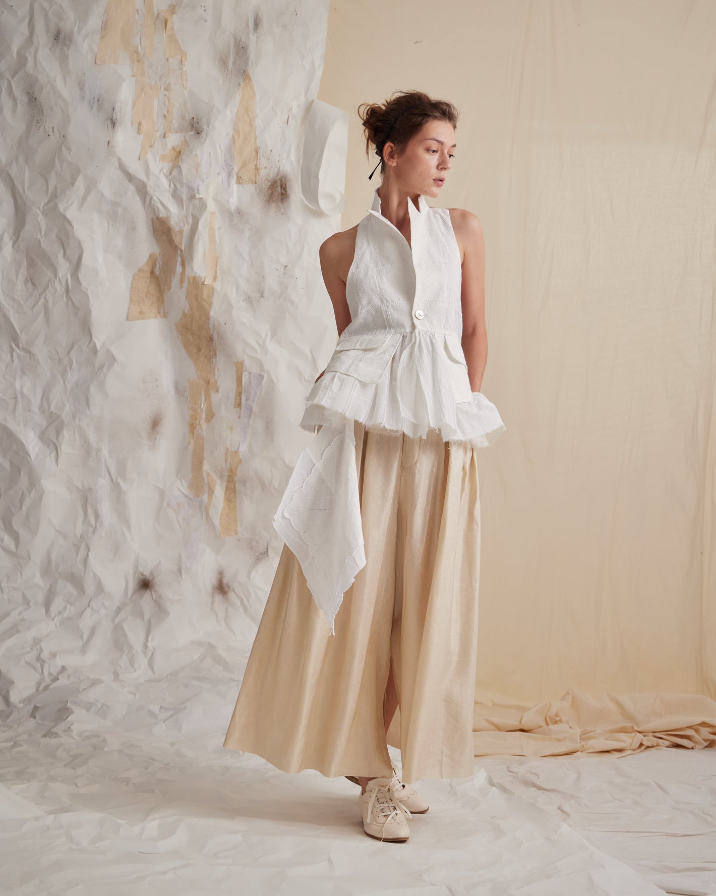 A Tentative Atelier SS23 Lookbook Womens white high neck waistcoat with a ruffle hem and beige wide leg trousers ensemble