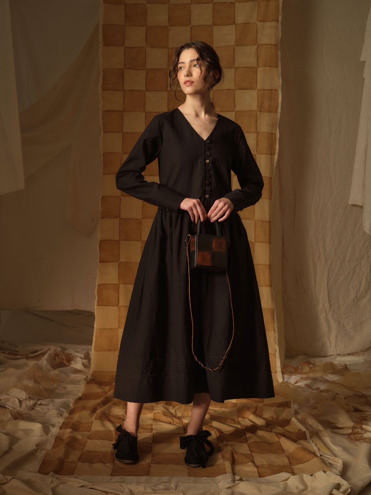 A Tentative Atelier AW21 Lookbook Womens black buttoned dress with long sleeves and check leather top handle bag