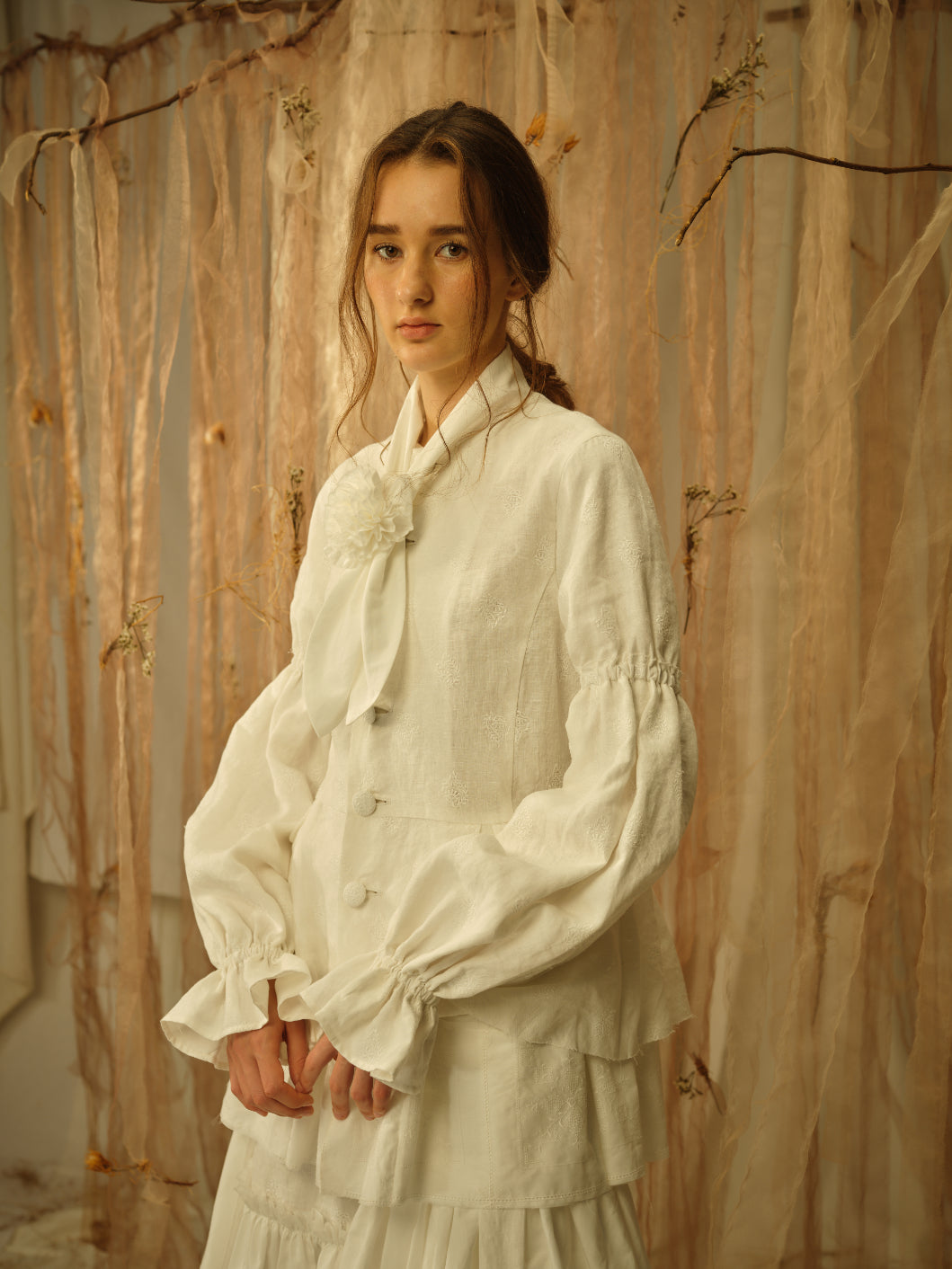 A Tentative Atelier SS21 Lookbook Womens crop of a white buttoned top with ruched sleeves and flower necktie