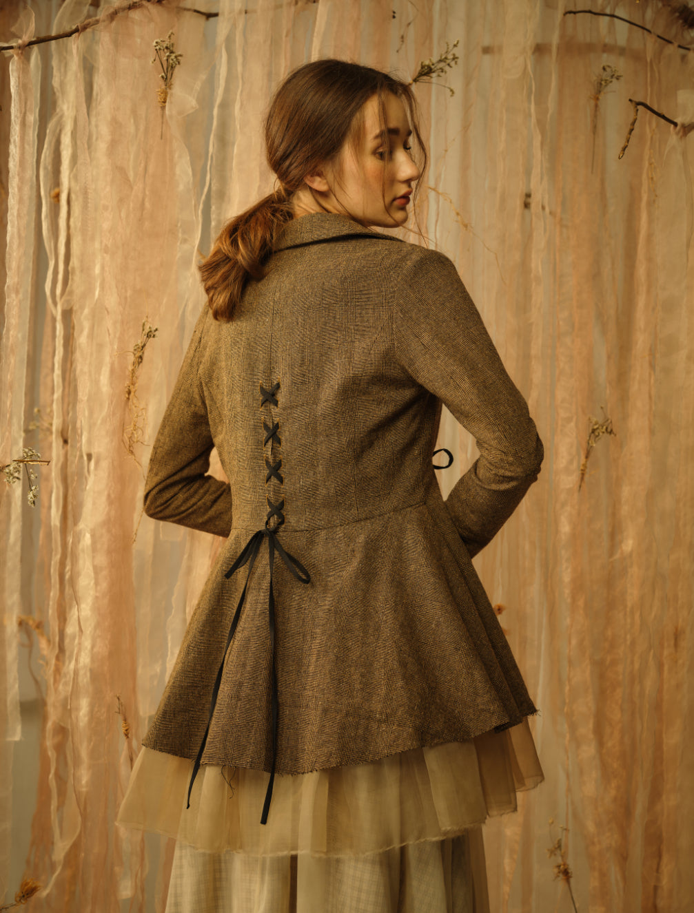 A Tentative Atelier SS21 Lookbook crop of Womens brown peplum jacket from the back, showing cross ribbon detailing