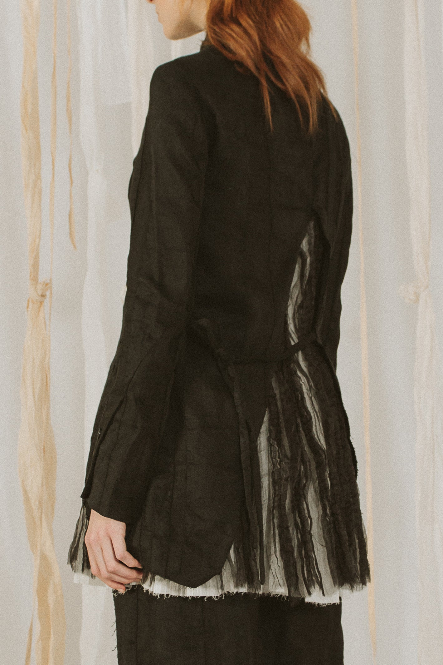 A Tentative Atelier SS18 Lookbook Womens crop of the back of a black jacket showing a high split hem inlaid with sheer black pleated silk