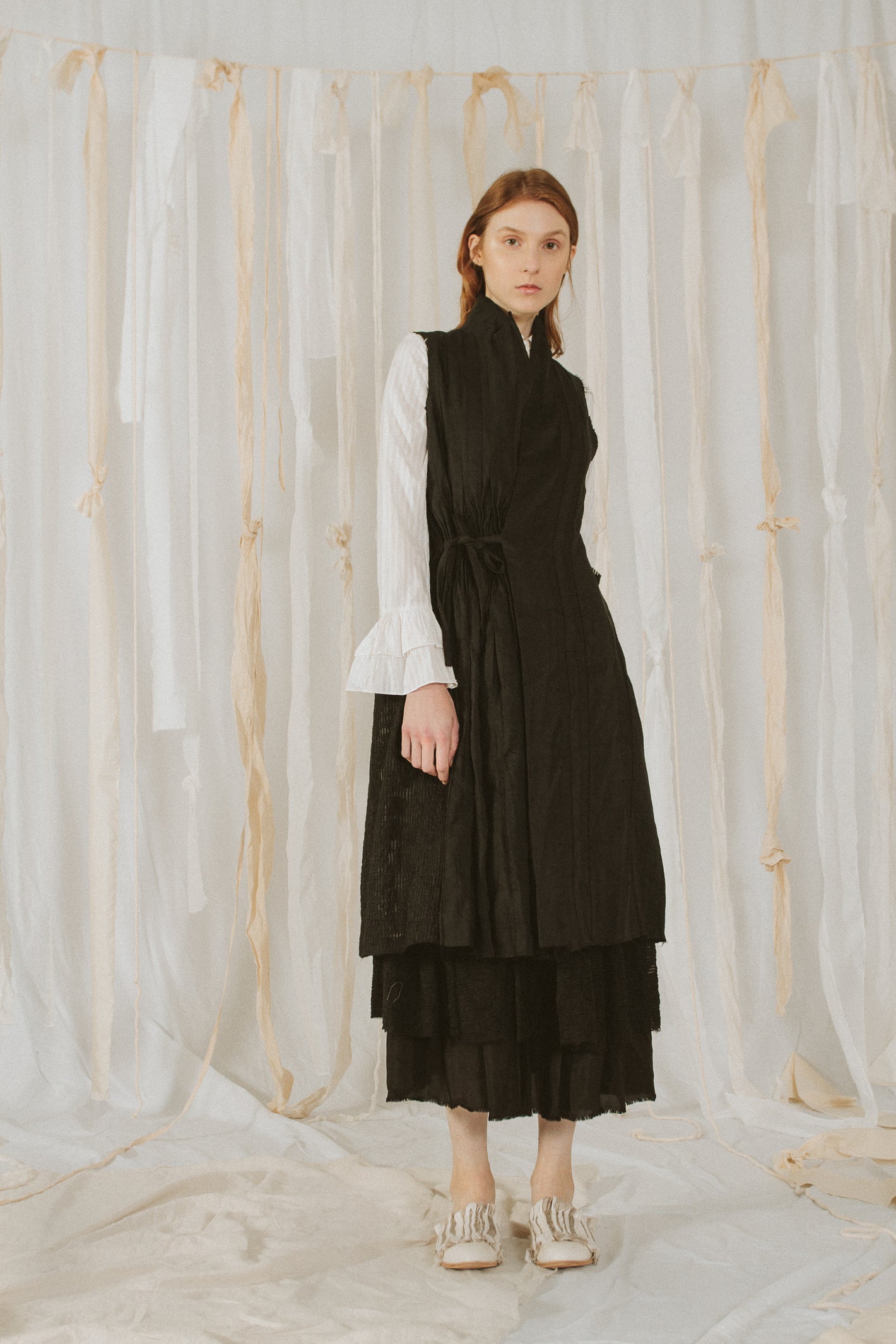 A Tentative Atelier SS18 Lookbook Womens black sleeveless high collar side fastening coat styled with a white shirt
