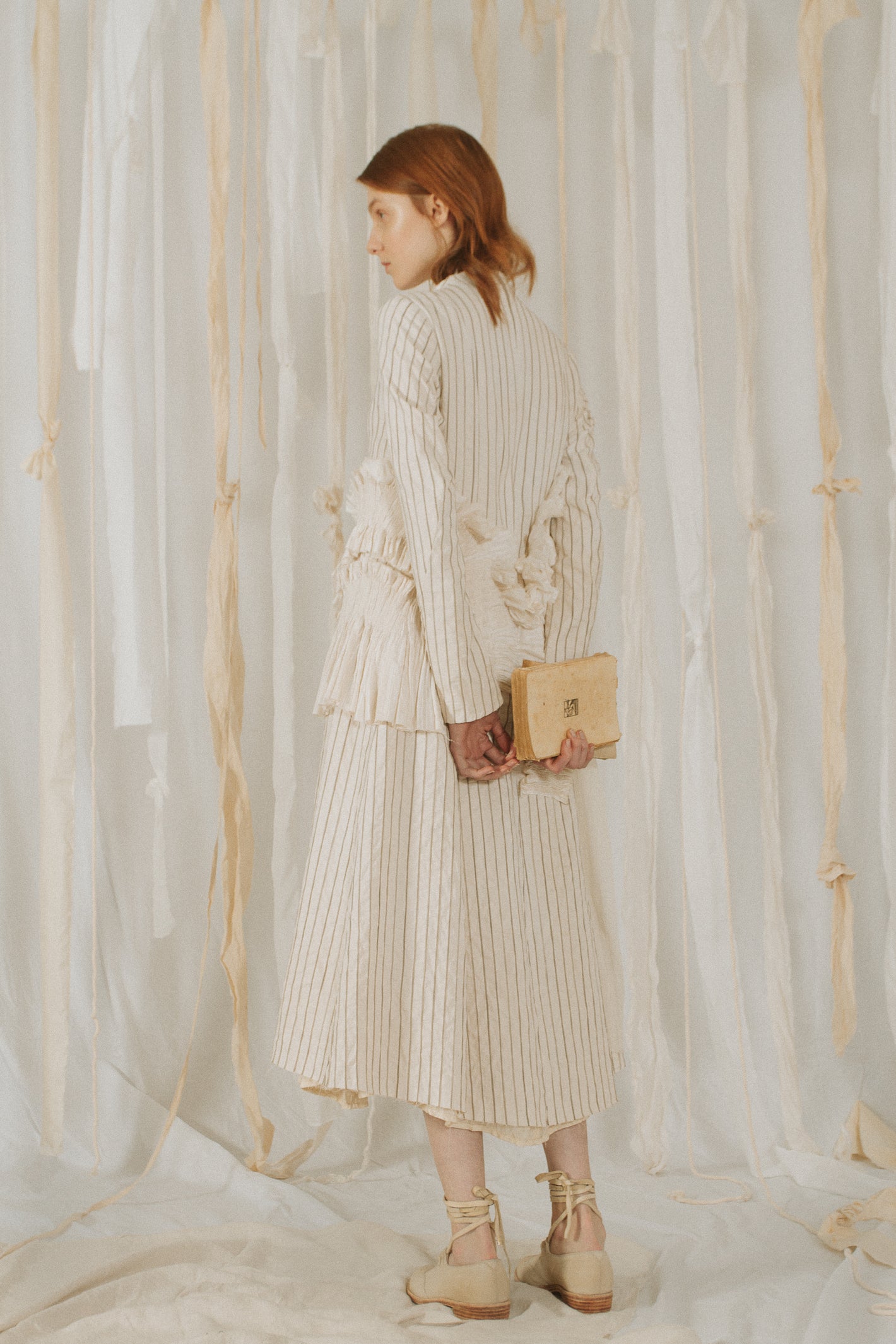 A Tentative Atelier SS18 Lookbook Womens crop of the back of a white collarless striped coat with smocked cloth appliqué