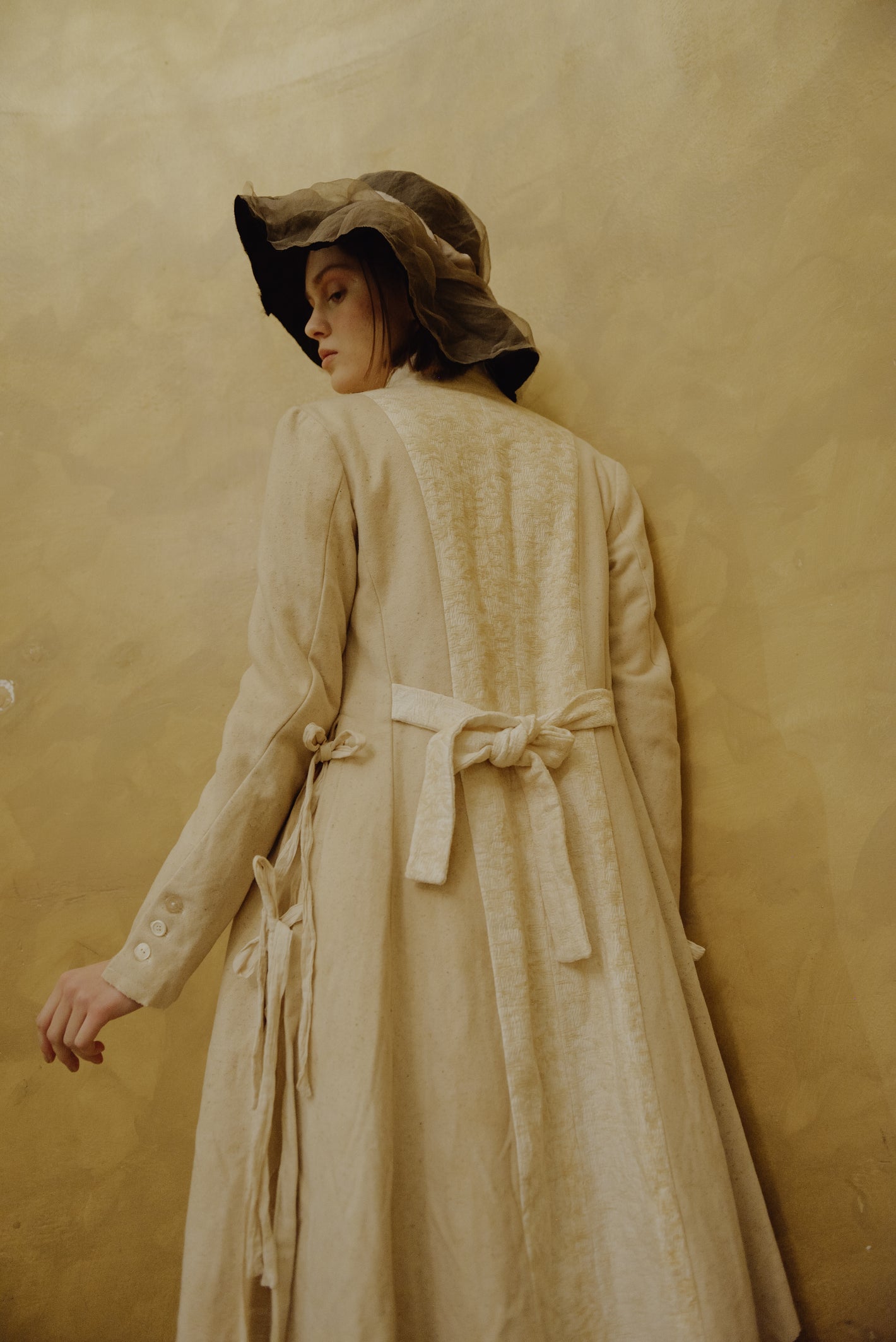 A Tentative Atelier AW19 Lookbook Womens crop of the back of a cream coat, showing its belted back and side ties