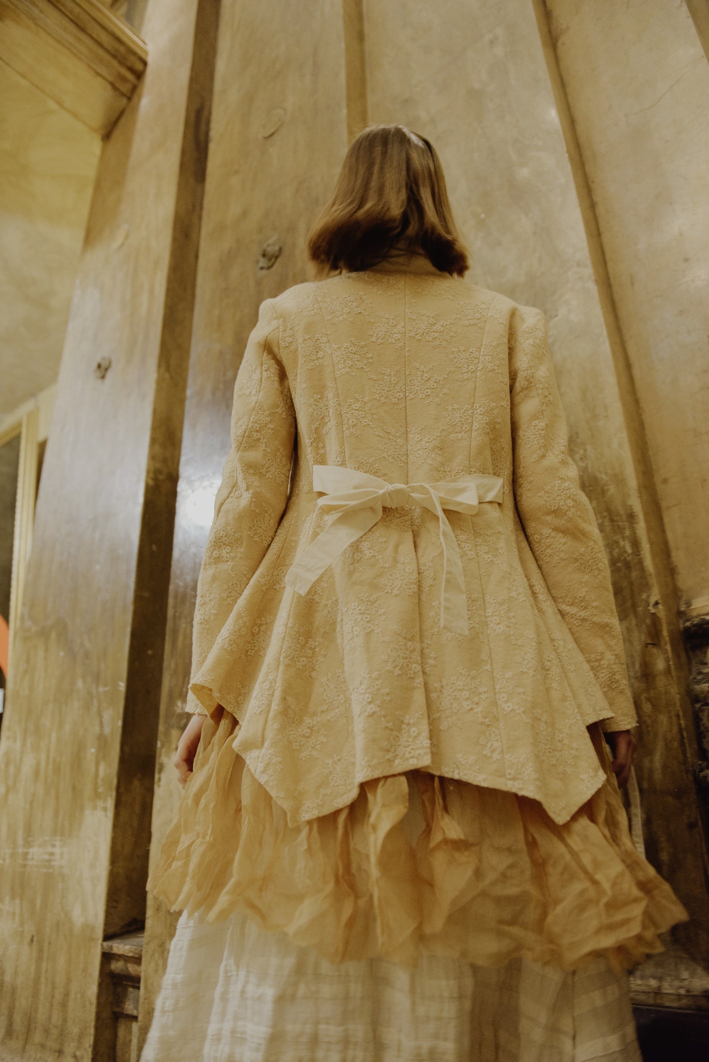 A Tentative Atelier AW19 Lookbook Womens crop of the back of a tailored cream jacket with a ribbon bow