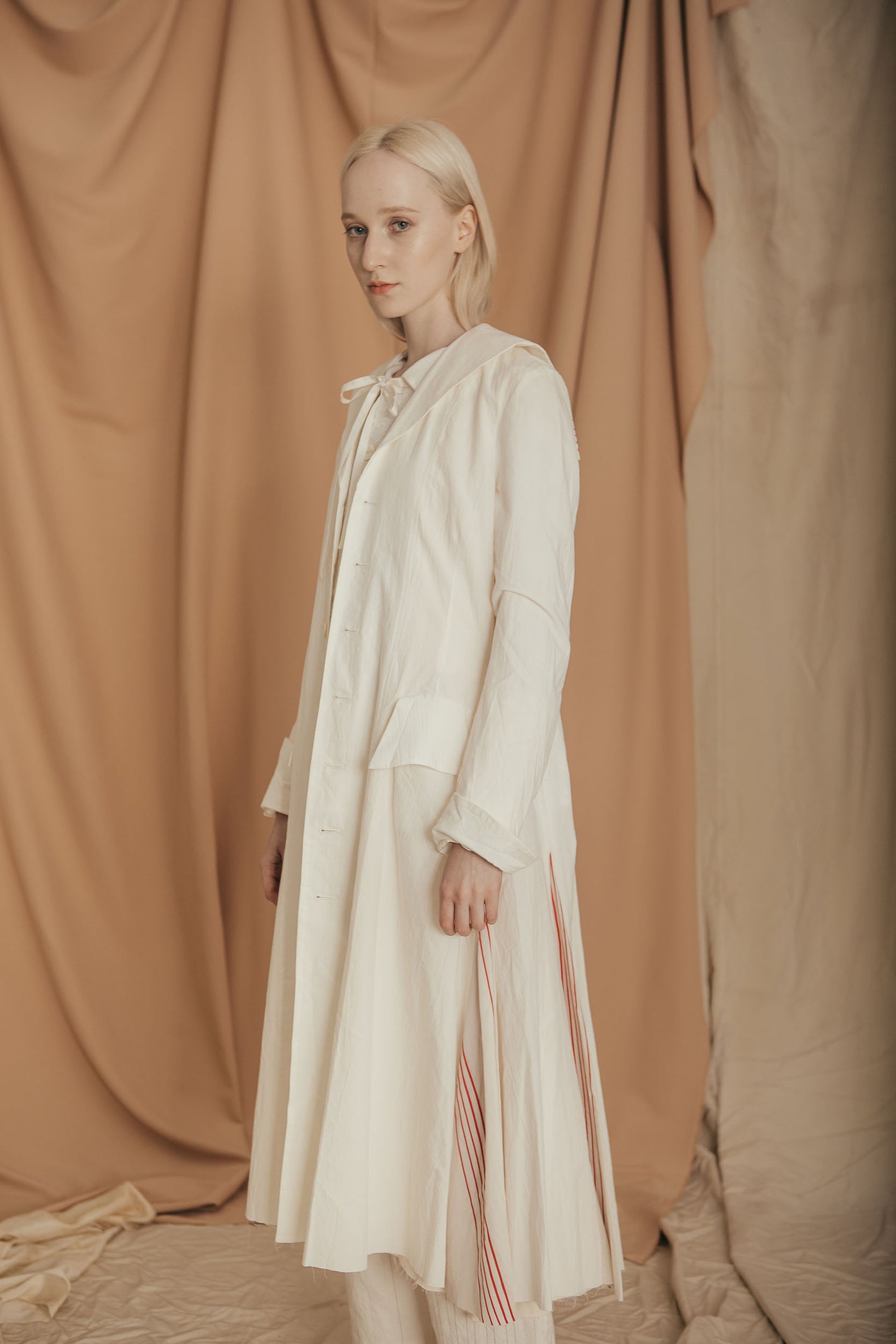A Tentative Atelier SS20 Lookbook Womens white coat featuring high split hems with red stripes
